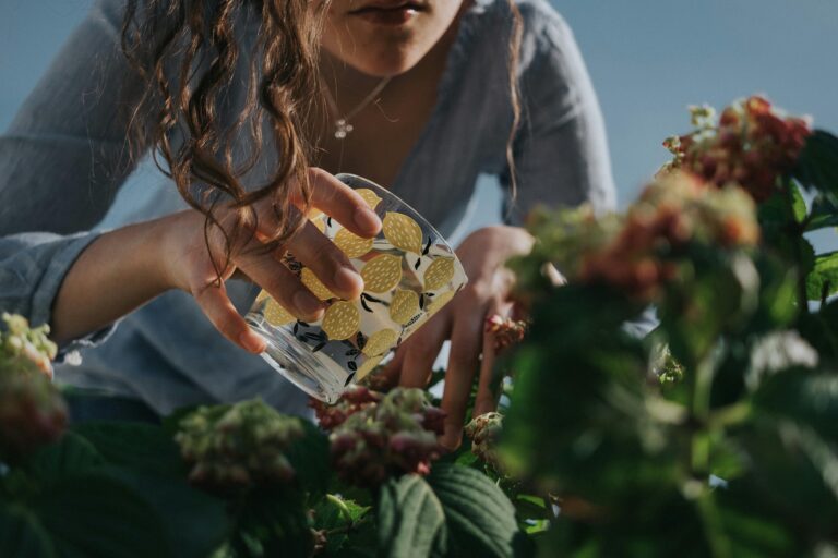Woman in a simple garden watering a plant with a glass